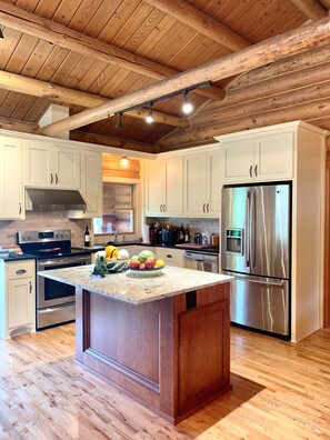 A modern kitchen with wooden beams, stainless steel appliances, and a central island with fruit. - Log Home on 9 acres (Chehalis)