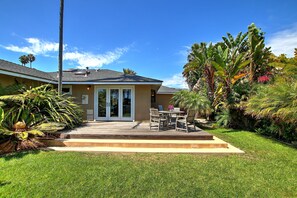Une maison dotée d’un patio, d’un coin repas et d’un jardin bien entretenu, agrémenté de diverses plantes et d’un palmier.