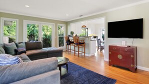 A spacious living room with a sofa, a coffee table, and a TV mounted on the wall. - Little Palm Cottage - Steps from Shoreline Park, walk to beach, live like a local (Santa Barbara)