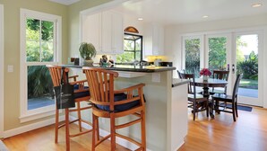 A kitchen with a central island, bar stools, and a dining table with chairs. - Little Palm Cottage - Steps from Shoreline Park, walk to beach, live like a local (Santa Barbara)