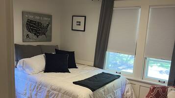 A bedroom with a bed, a window with blinds, a ceiling light, a wall map, and a framed picture.