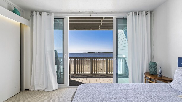 Une chambre avec un lit, une table de chevet et une vue sur la plage, accessible par une porte-fenêtre coulissante.