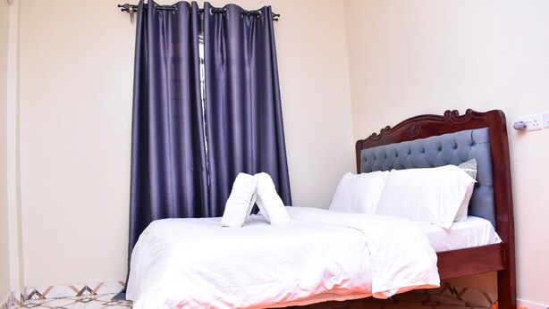 A neatly made bed with white linens and a single pillow, a dark blue curtain, and a patterned floor. - KJ'S where Cosy Memories last. (Meru)