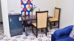 A compact living space with a dining area featuring a small table and two chairs, a refrigerator, and a decorative wall panel. - KJ'S where Cosy Memories last. (Meru)