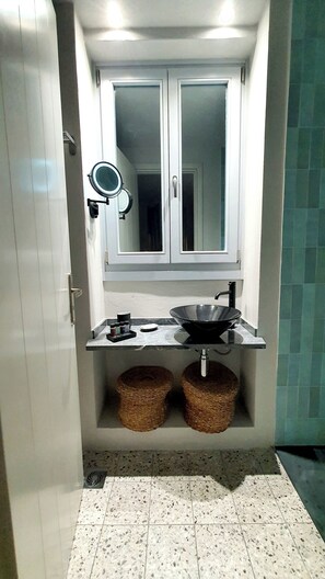 Une salle de bain avec un meuble-lavabo blanc, un miroir rond, un lavabo noir et deux paniers en osier.