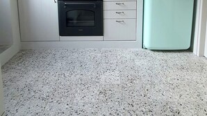 Een kleine keuken met witte kastjes, een zwarte oven, een blauwgroene koelkast en een terrazzovloer.