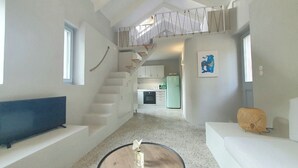 Een modern interieur met een trap naar een hoger niveau, een keukenhoek en een zithoek met een bank en een decoratief object.