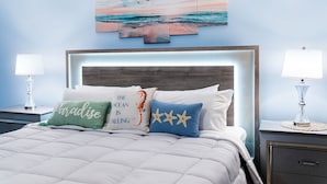 Quarto com cama, duas mesas de cabeceira, um criado-mudo, uma obra de arte na parede e um quadro emoldurado.