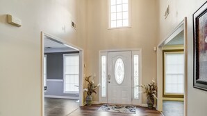 Um corredor com piso de madeira, uma porta branca com painel de vidro decorativo e duas plantas em vasos de cada lado.