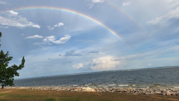 Un paysage côtier avec un arc-en-ciel au-dessus de la mer, une côte rocheuse et une zone herbeuse.