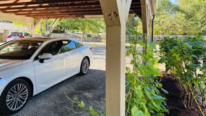 Un coche blanco estacionado bajo una pérgola de madera con un camino de grava.