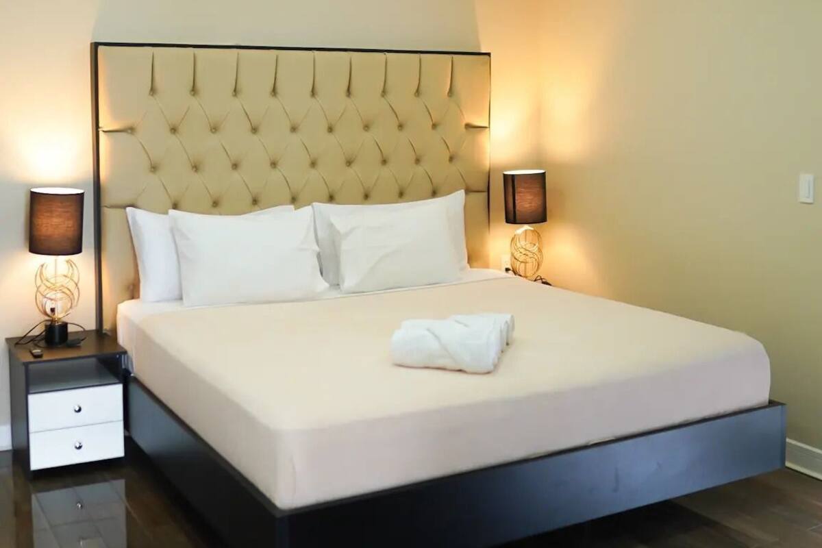 A neatly made bed with a tufted headboard, two bedside tables with lamps, and a wooden floor.