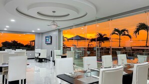 Ein Restaurant mit Blick auf den Sonnenuntergang, mit weißen Stühlen und Tischen mit Weingläsern.