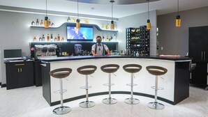 Eine moderne Bar mit gebogenem Tresen, mehreren Hockstühlen und einem Fernsehbildschirm.