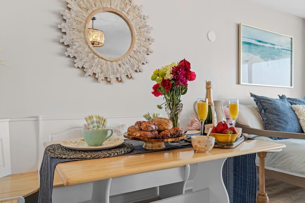 Une table dressée pour le petit-déjeuner, avec des viennoiseries, des fleurs et des boissons, dans une pièce où se trouvent un lit et un tableau accroché au mur.