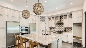 Una cocina moderna con armarios blancos, una isla central con taburetes de bar, un refrigerador de acero inoxidable, un horno y un salpicadero decorativo.