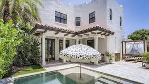 Una piscina con una sombrilla blanca, un porche cubierto y un edificio blanco con varias ventanas.