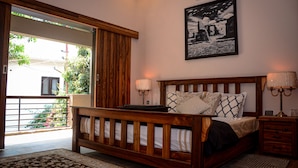 Un dormitorio con cama de madera, lámparas de noche, un cuadro en la pared y vistas al exterior a través de una puerta corredera.