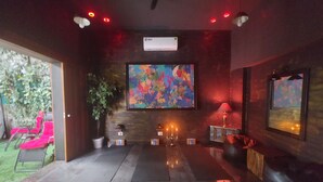 Una sala de estar moderna con un televisor grande, una chimenea y una zona de estar con sillas rojas.