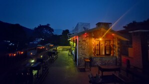 Un edificio de piedra con zona de bar, mesas al aire libre y vistas a las montañas al fondo.