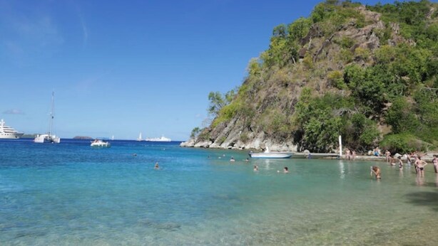 A beach with clear turquoise water, boats, and people swimming.