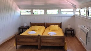 A room with two wooden beds, white walls, and a window with a view of greenery.