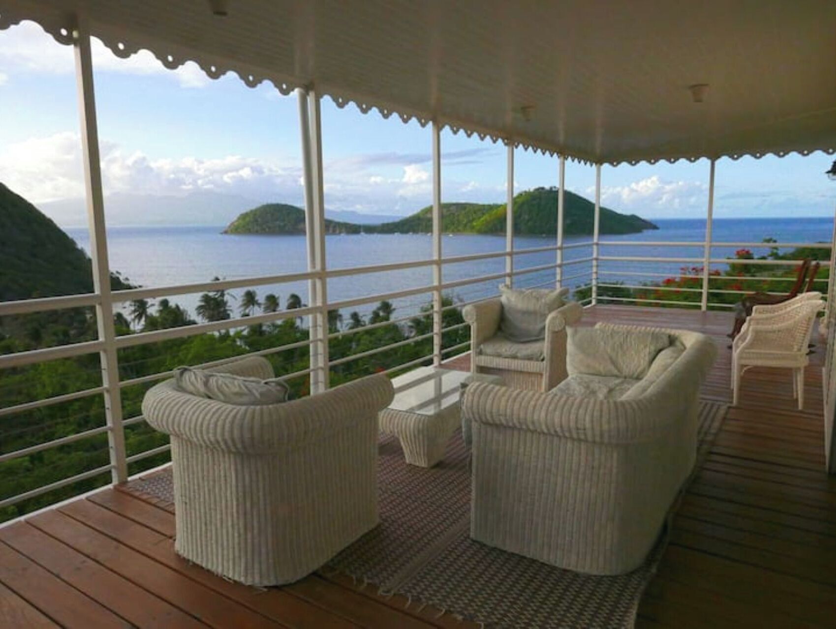 A covered outdoor seating area with wicker furniture and a view of the sea and islands.