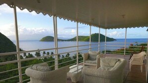 A covered outdoor seating area with wicker furniture and a view of the sea and islands.