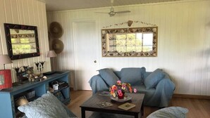 A living room with a blue sofa, a coffee table with a vase of flowers, a bookshelf, and a door with a mirror above it.