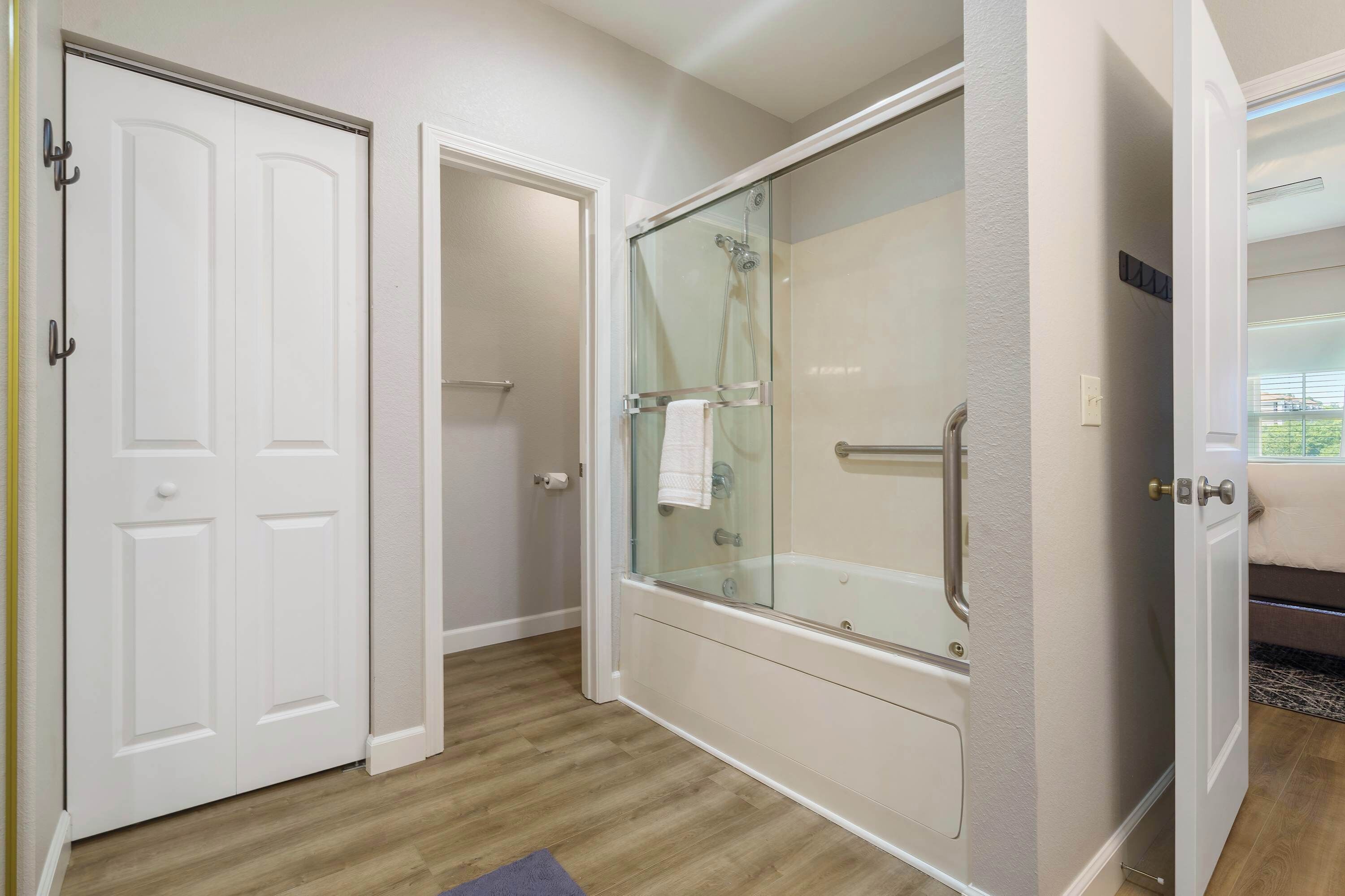 A bathroom with a glass-enclosed shower, a white door, and a wooden floor.