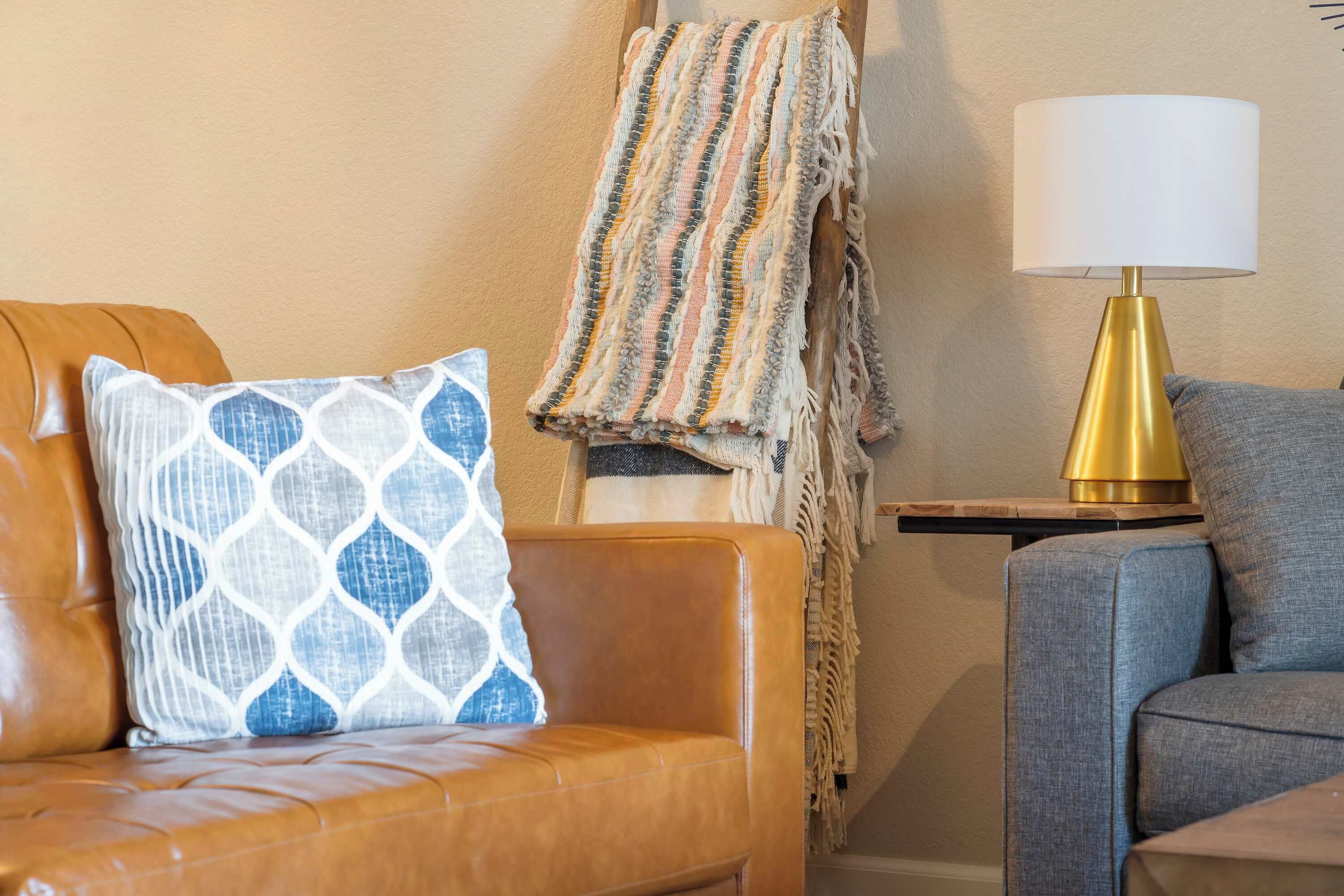 A cozy living room with a brown leather sofa, a patterned throw blanket, and a gold lamp on a wooden side table.