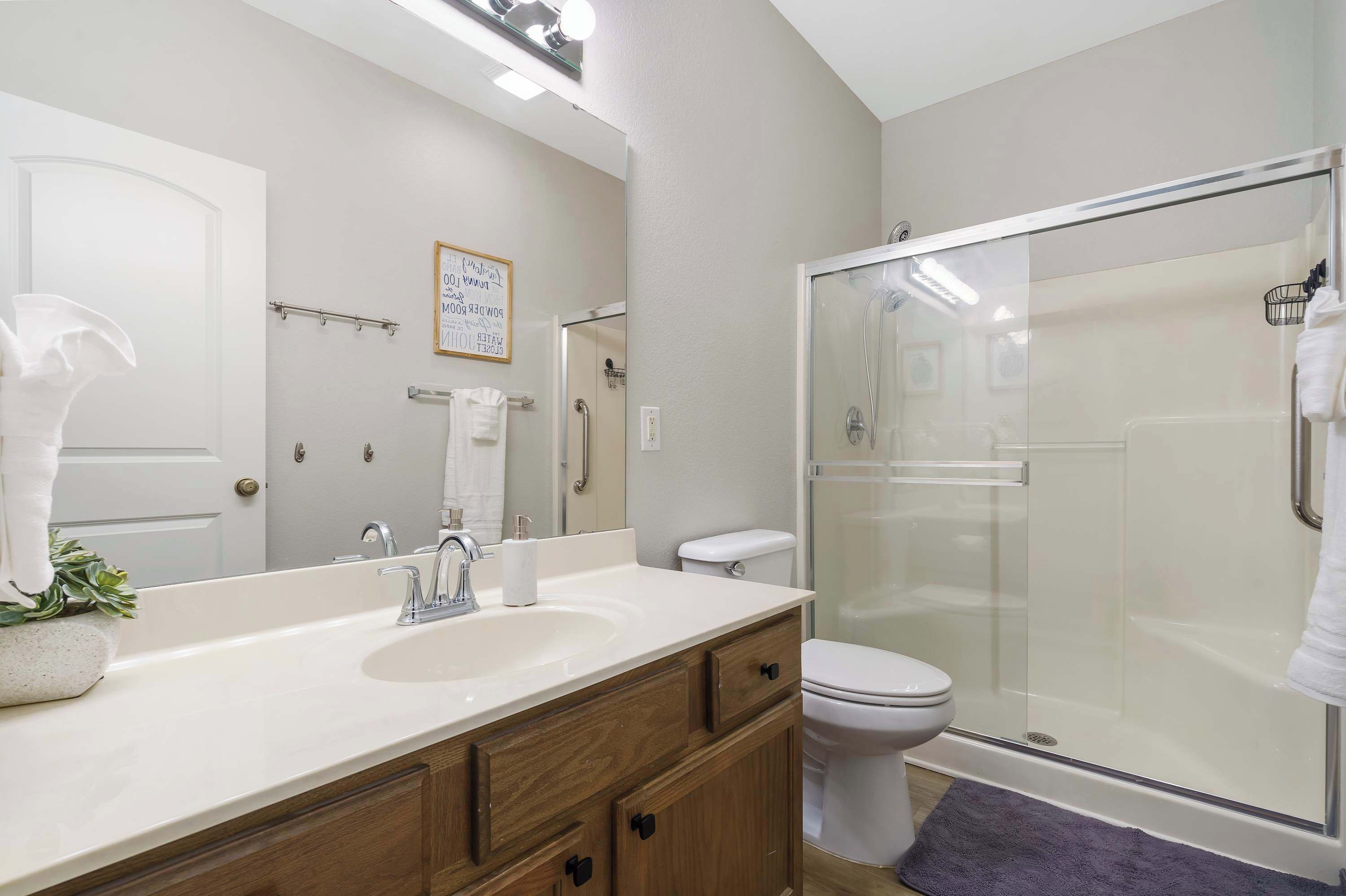 Une salle de bain moderne avec un lavabo blanc, un meuble-lavabo en bois, des toilettes et une douche à parois de verre.