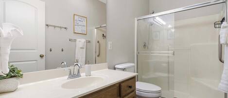 Une salle de bain moderne avec un lavabo blanc, un meuble-lavabo en bois, des toilettes et une douche à parois de verre.