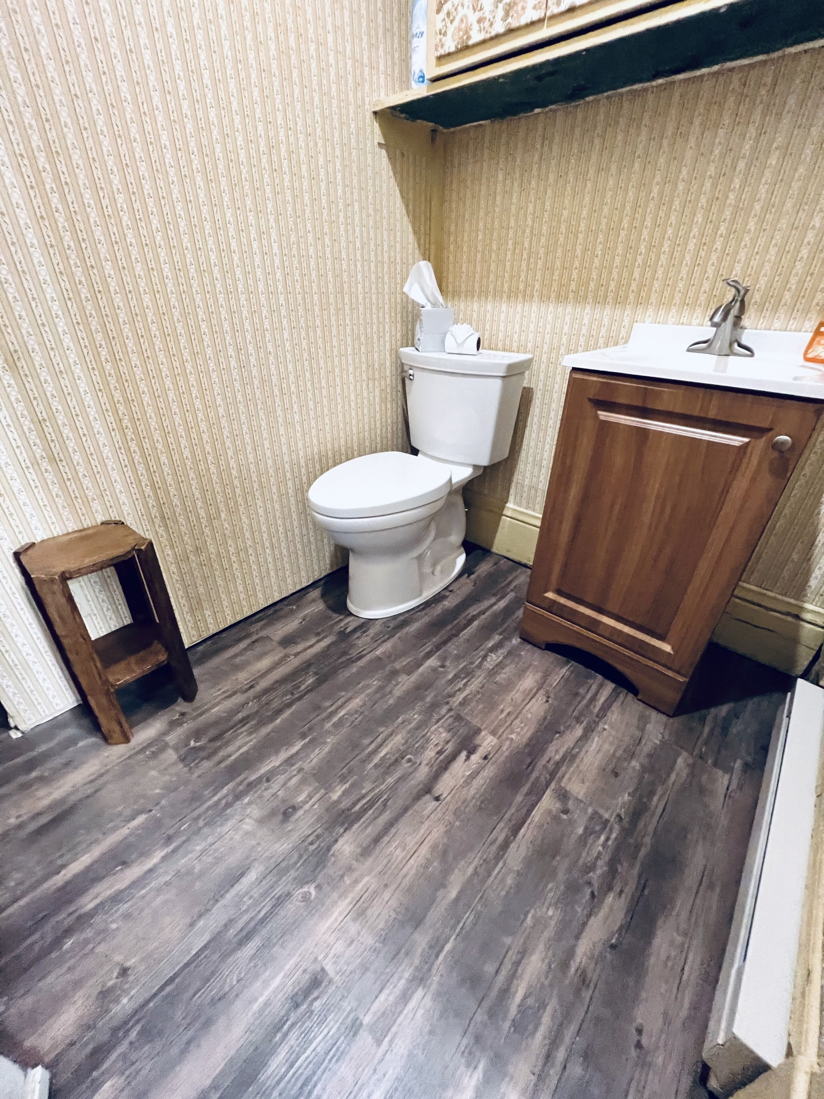 A bathroom with a toilet, a wooden cabinet, and a small wooden stool.