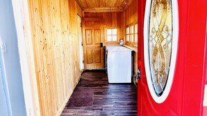 A narrow hallway with wooden walls and a red door with a decorative window. A white washing machine is visible in the background. - Charming Country Victorian Farm House (Barton)