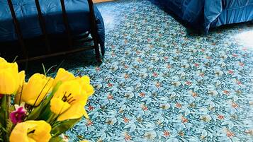 A room with two beds, a window with curtains, and a floral-patterned floor.