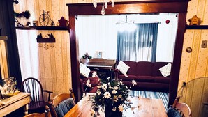 A dining room with a wooden table, chairs, a chandelier, and a piano in the background. - Charming Country Victorian Farm House (Barton)