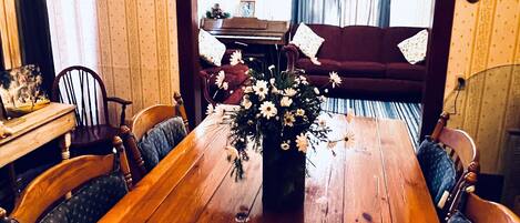 Un comedor con una mesa de madera, sillas, una araña y un piano al fondo.