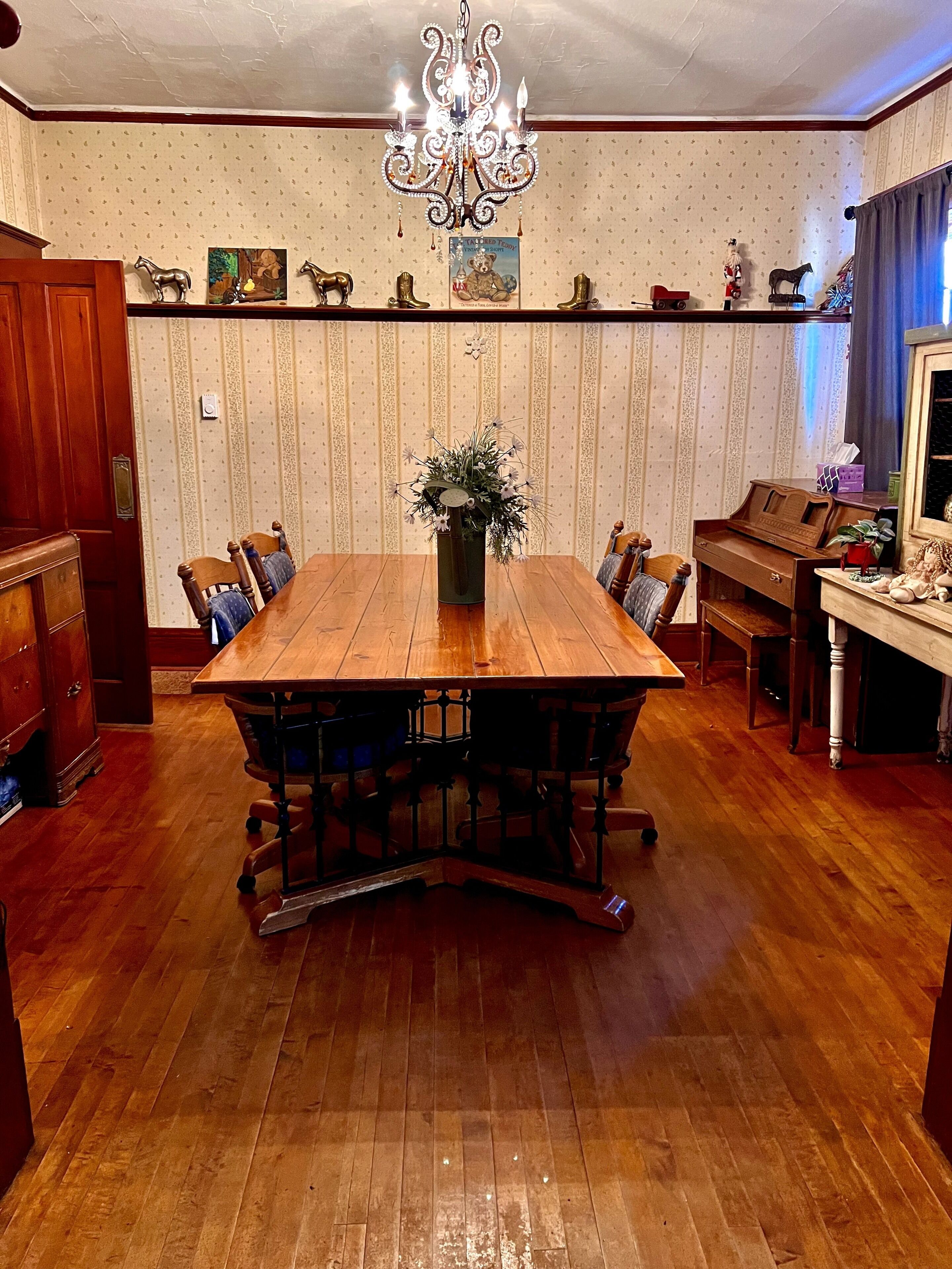 A dining room with a wooden table, chairs, a chandelier, and a piano.