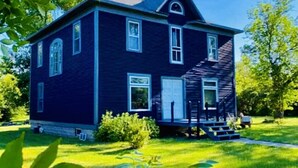 A two-story house with a dark blue exterior, a front porch, and a well-maintained lawn. - Charming Country Victorian Farm House (Barton)