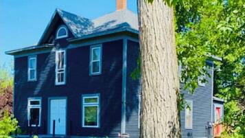 A two-story house with a dark exterior, a visible chimney, and a large tree in the foreground.
