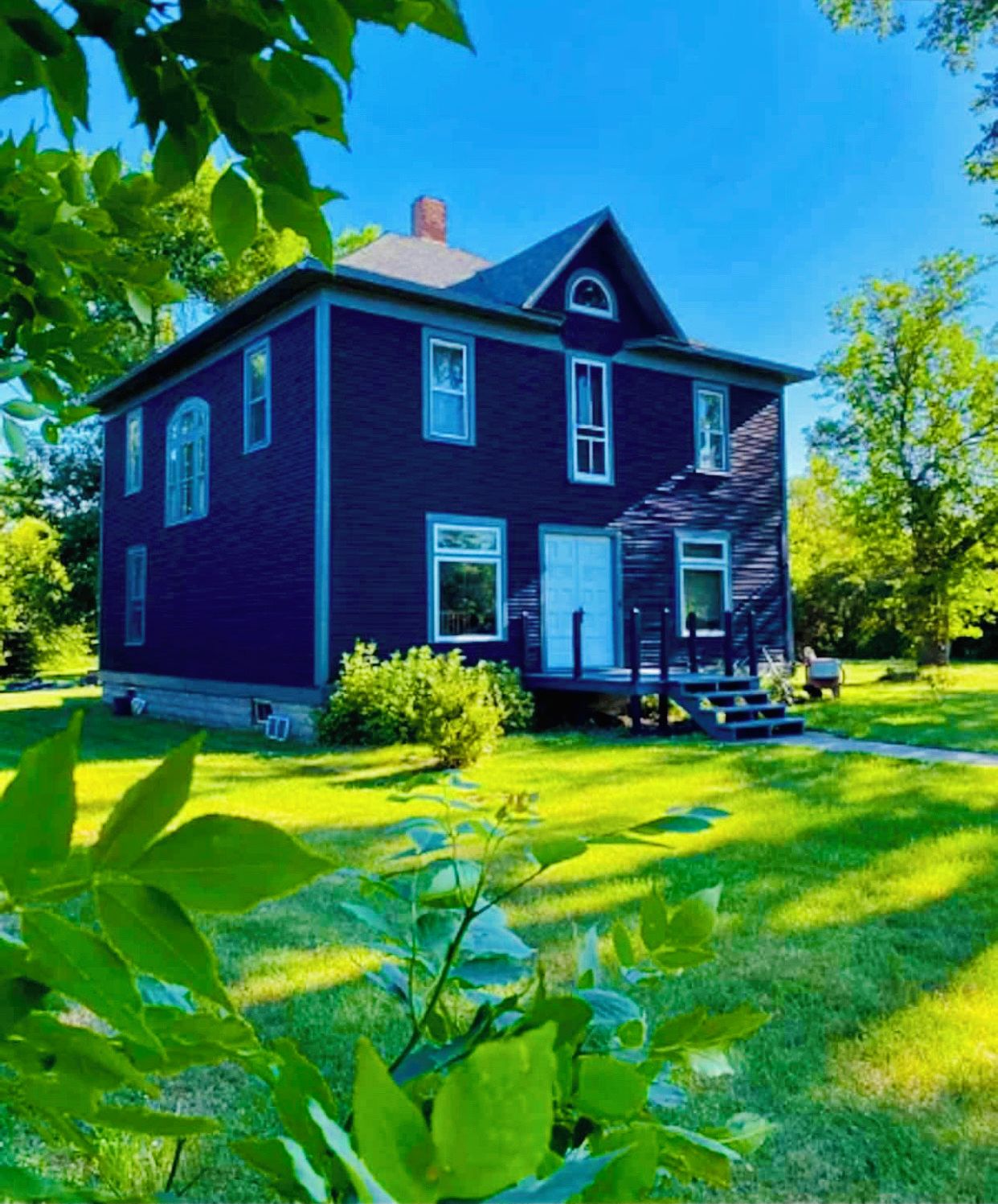 A two-story house with a dark blue exterior, a front porch, and a well-maintained lawn.