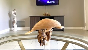 Una sala moderna con un televisor de pantalla plana montado en la pared, una escultura de madera sobre una mesa de vidrio y un adorno en la pared.