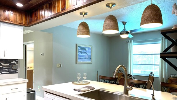 Una cocina moderna con una isla central, pileta de acero inoxidable y lámparas colgantes tejidas.