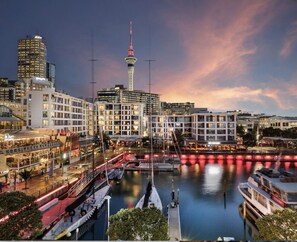 A waterfront cityscape with modern buildings, a prominent tower, and a marina with boats. - Penthouse Premier - Sebel (Auckland)