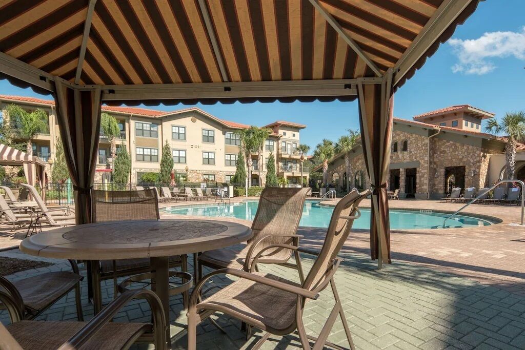 A covered outdoor area with a pool, lounge chairs, and a table.