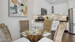 Una cocina moderna con armarios blancos, una mesa de comedor de vidrio, sillas de mimbre y un refrigerador de acero inoxidable.