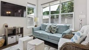 Una sala de estar con un sofá azul claro, un televisor de pantalla plana, una lámpara y una silla de mimbre.