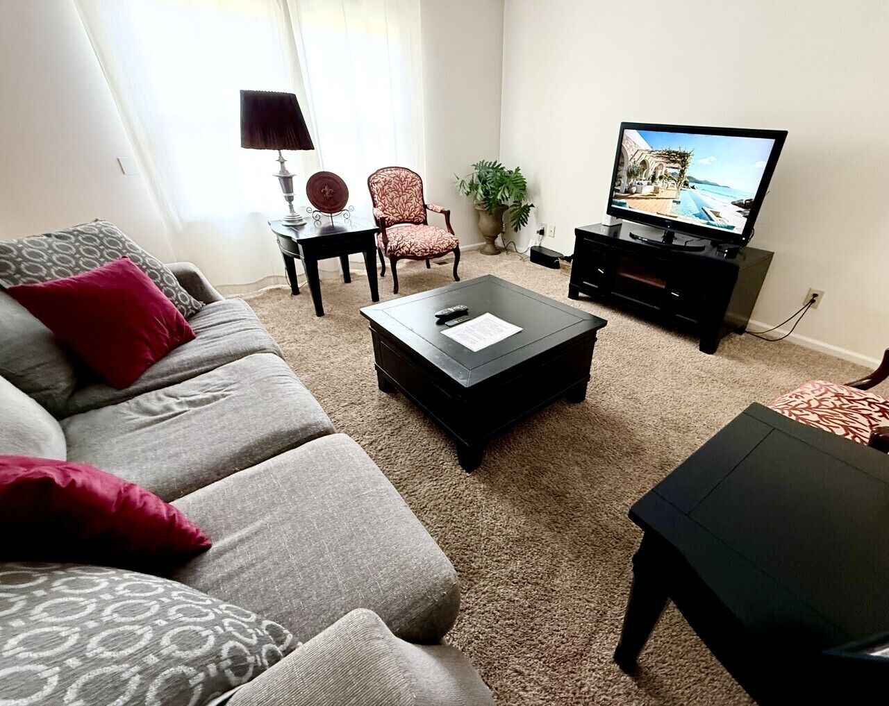 Una sala de estar con un sofá, una mesa de centro, un televisor, una lámpara y una silla.