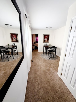 A room with a dining table, chairs, and a mirror reflecting the room. There is a door on the right and a window on the left. - Cozy Downtown Destination (Raleigh)